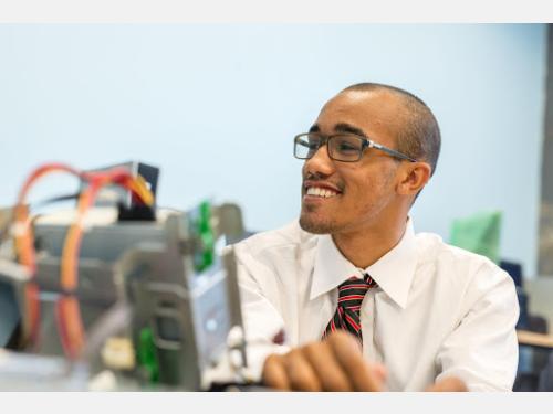 Smiling student holds up computer parts.