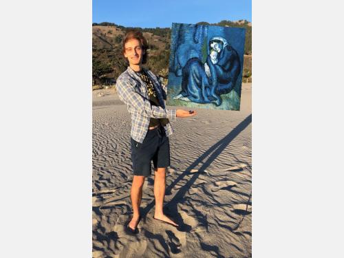 In this photomontage, a young man stands on a windswept beach, looking out at us with a smile. He gestures toward a floating modern painting. Mostly blue, it shows a long-limbed woman cradling a baby as she rests on the floor in a corner.