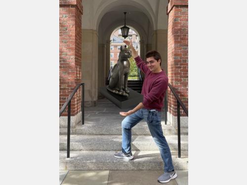In this photomontage, Paul Tamburro stands on steps in front of a series of archways. He gestures toward a leaded bronze sculpture of a cat from ancient Egypt (mid-7th to late 1st century BCE), which is featured on his tour.