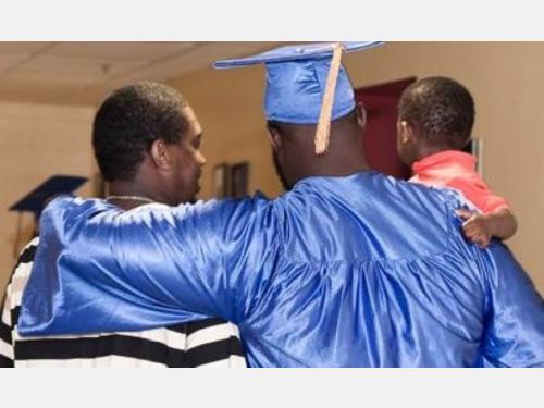 High school graduate in cap and gown has his arms around family members
