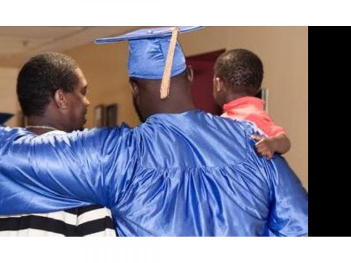 High school graduate in cap and gown has his arms around family members