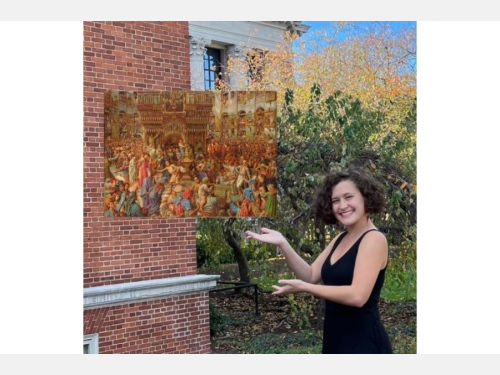 A smiling young woman stands outside a brick building gesturing toward a painting that appears to float beside her. The painting depicts, in mostly gold tones, throngs of visitors to an ornate religious structure.