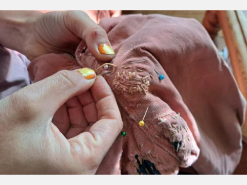 Close-up of hands mending pink pants; the embroidered threads are of various colors.