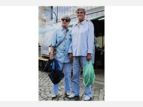 Two women in matching outfits stand close together in a city setting.