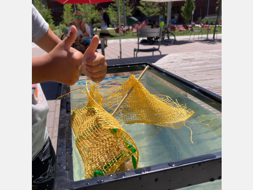Kid gives thumbs up next to the floating wetlands craft in the Kendall/MIT Open Space