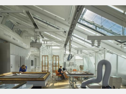 Two conservators work on respective artworks in their large laboratory space, which is illuminated by natural light.