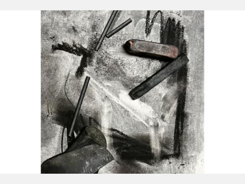 A close-up of an abstract charcoal drawing with several charcoal sticks and crayons strewn across it.