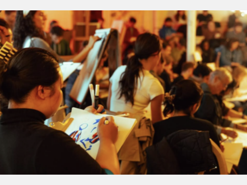 A large group of people sit or stand sketching on drawing pads. 