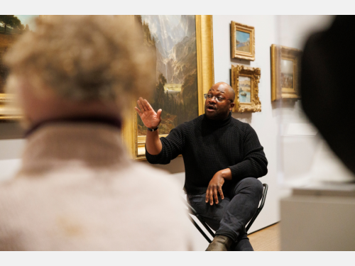 Horace Ballard seated in a gallery discussing a painting with visitors.