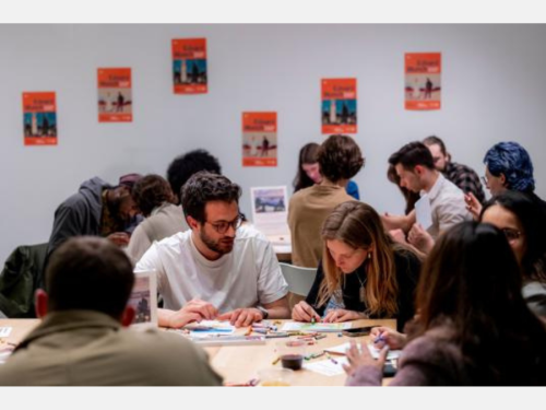 A group of people enjoying a coloring activity with bright orange posters in the background.