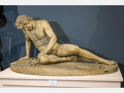 Image of the plaster cast of a statue of a man in the nude lying in pain on a shield with his sword nearby.