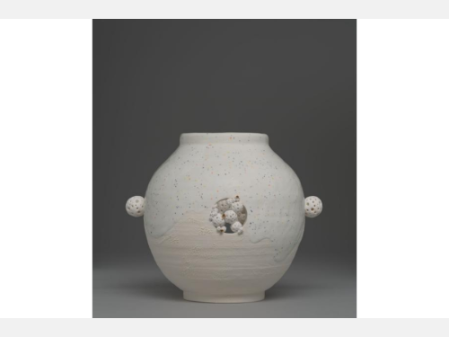 A white vase, partially glazed in confetti and gold glaze, features a small ball on each side and in the center front a group of smaller ones.