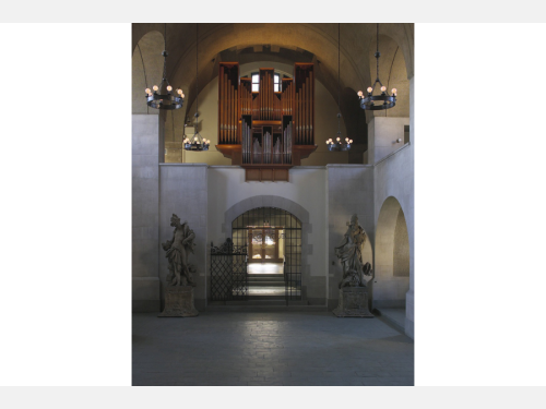 A room with several arches and figural statues in the corners with an organ musical instrument in the center.
