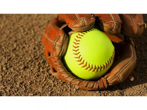 yellow softball in a glove on infield dirt