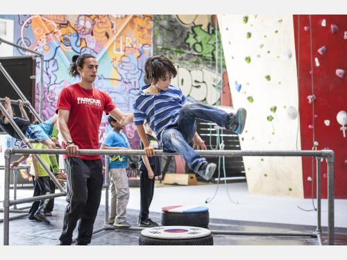 Photo of parkour instructor assisting a child jump over a high bar structure.