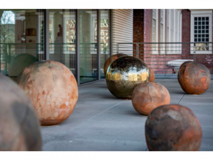 Several terracotta spheres and one gold sphere installed on an enclosed terrace.
