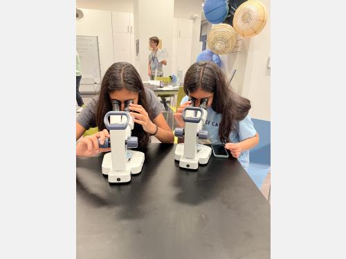 two teens looking into optical microscopes at a black lab table