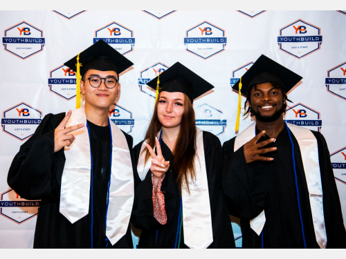 Three 2023 YouthBuild Graduates pose in their caps and gowns.