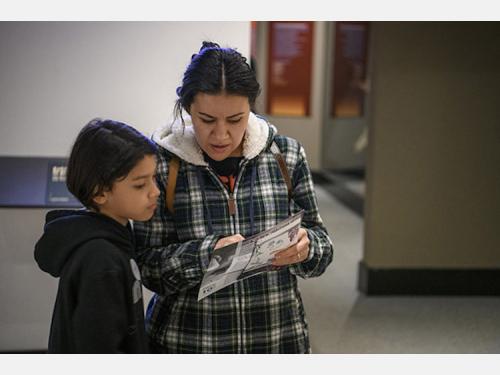 a woman in a plaid jacket and a child in a black hoodie look at a museum map in a gallery