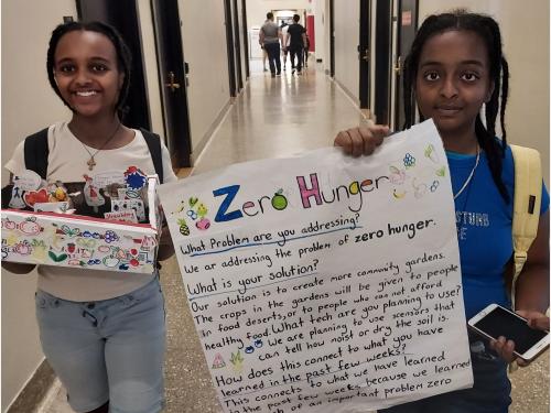 Photo of students walking together with their diorama and a poster discussing "Zero Hunger" at MIT Full STEAM Ahead Into Summer program.