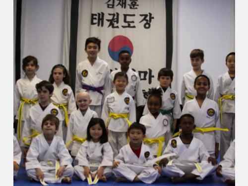 A group of martial arts students with yellow belts standing and smiling together for a photo.