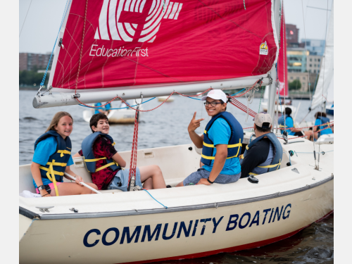 Photo of students smiling and waving from a Community Boating sailboat.